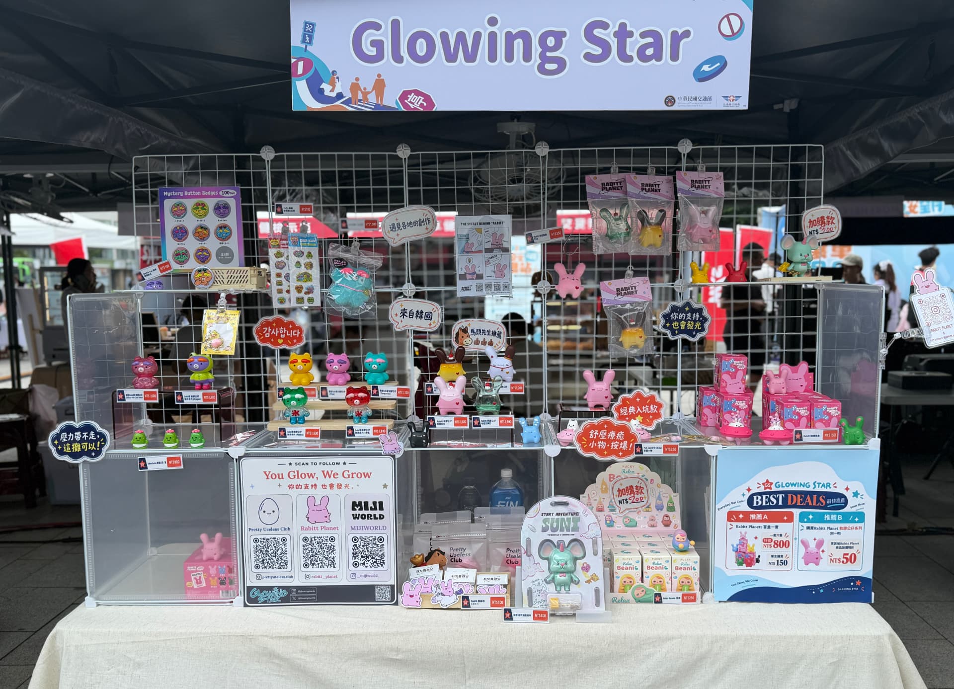 The Glowing Star booth at 交安祭 in Taichung, with the overhead brand sign above wire racks and acrylic risers holding Rabitt Planet, Pretty Useless Club and MIJI WORLD figures, badges and blind boxes