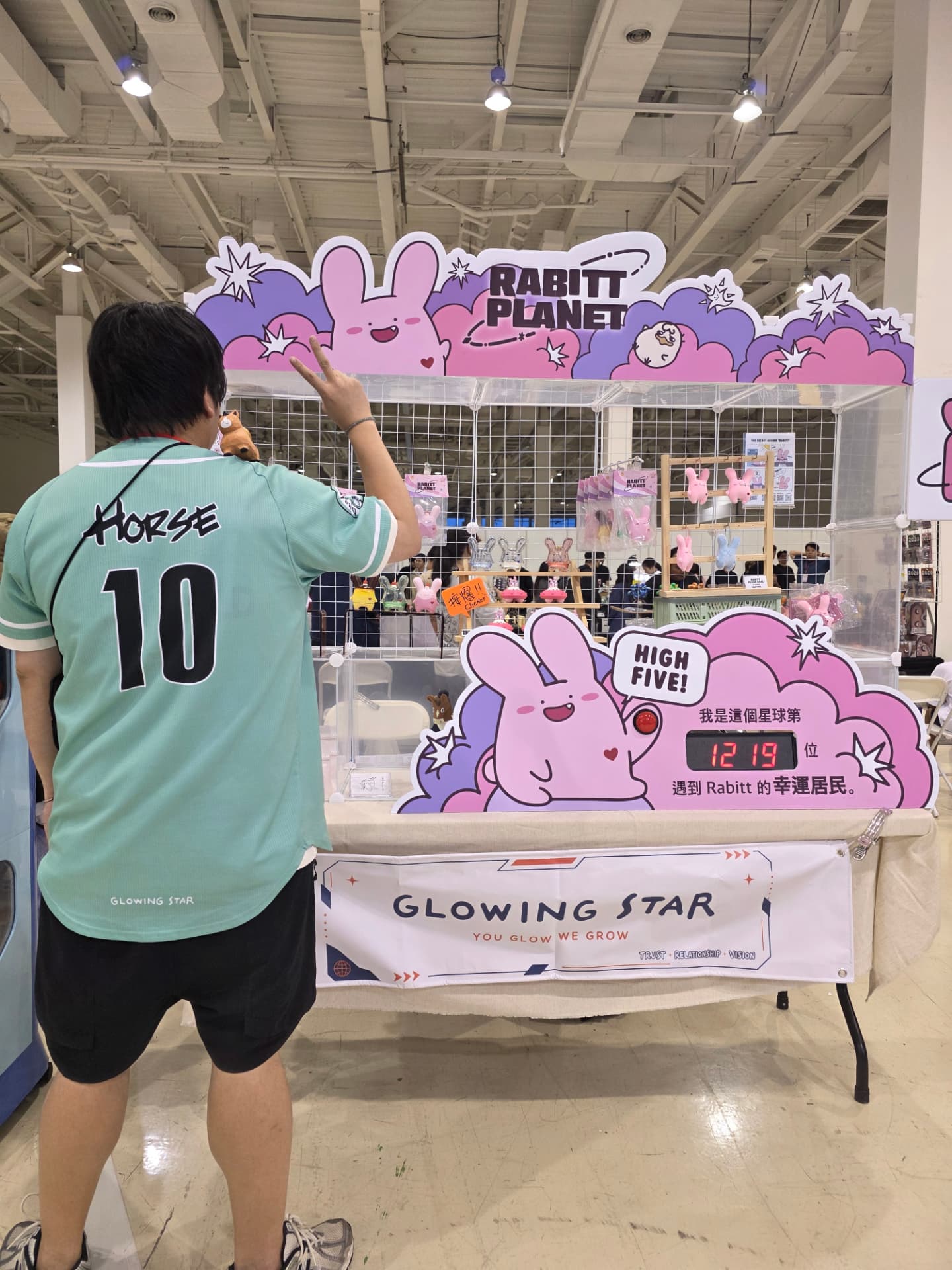 A visitor raising a hand in front of the Rabitt Planet booth at the Toy Life Festival in Kaohsiung, with the high-five counter reading 1219