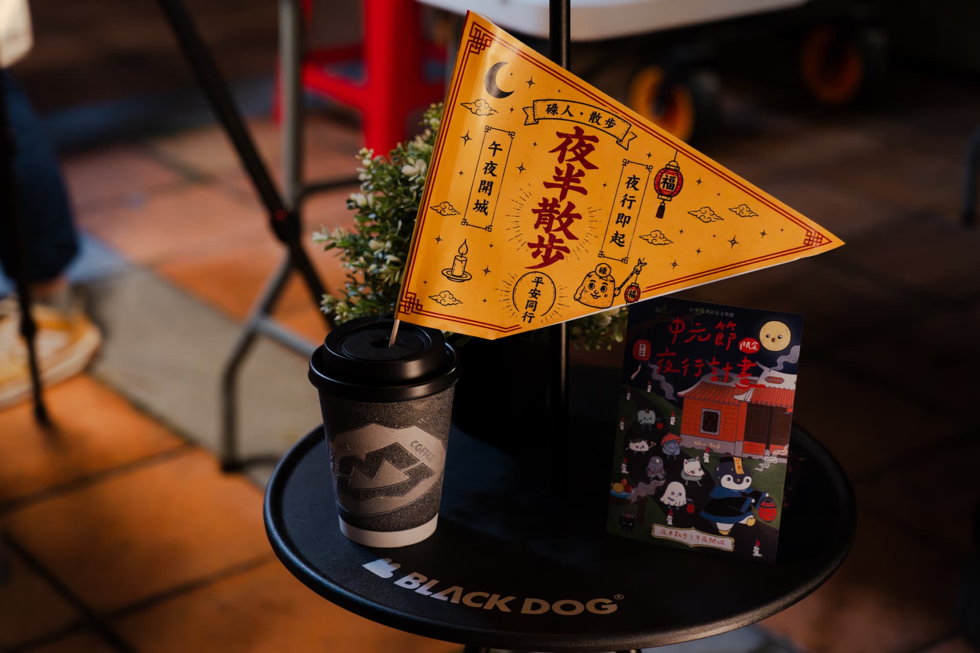 A 夜半散步 pennant flag and the Zhongyuan Festival night-walk postcard arranged on a Black Dog coffee table at the Taiwan Folk Arts Museum